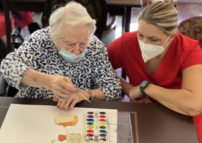 rehab staff crouching beside a patient painting a craft
